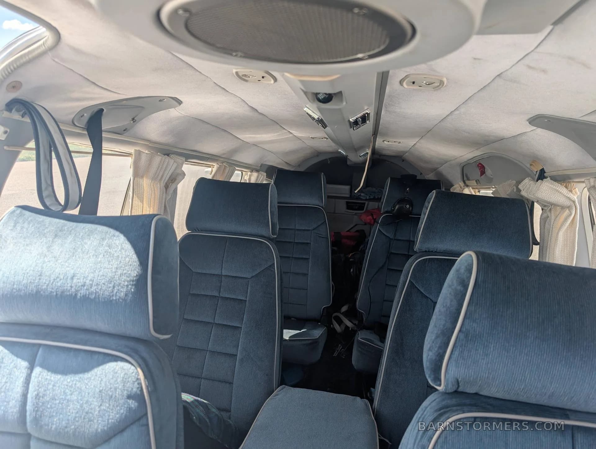 The interior cabin of the aircraft, showing rows of blue upholstered seats and the overhead panel.