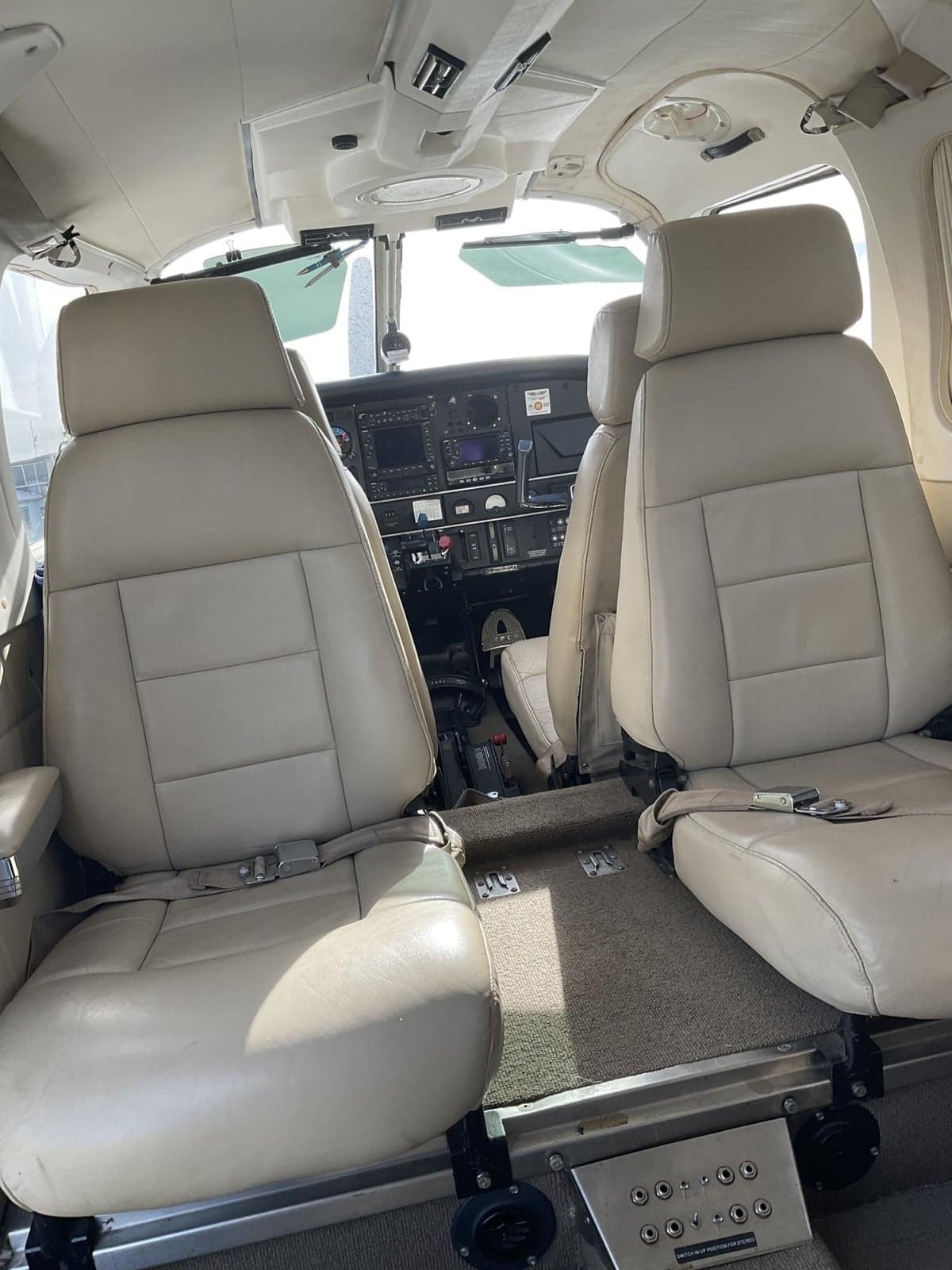 The interior cabin of a Piper Saratoga aircraft with light beige leather seats and a view towards the cockpit.