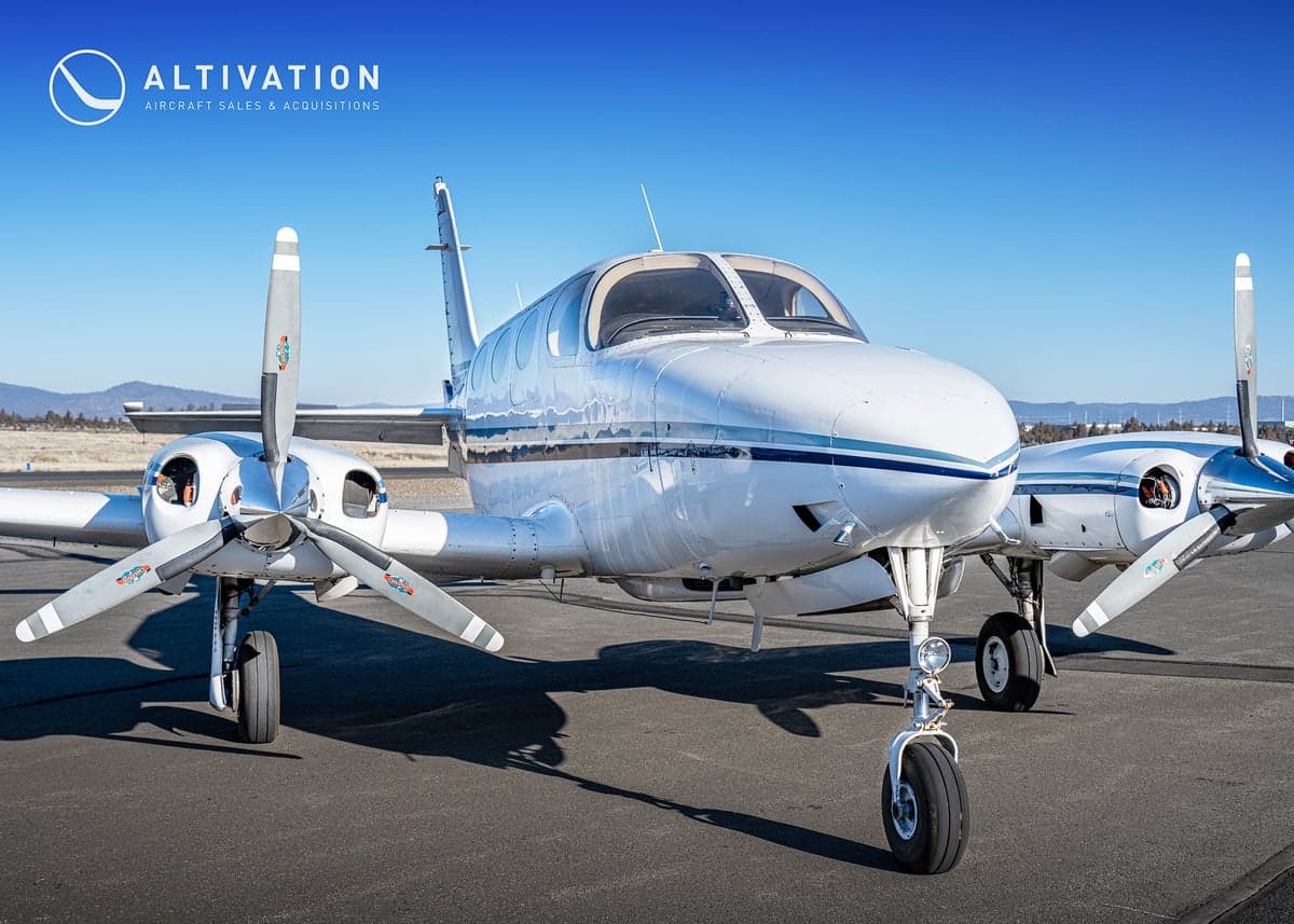 Close-up of the front of a white and blue twin-engine aircraft, registration N7719Q, showing the nose and propellers.