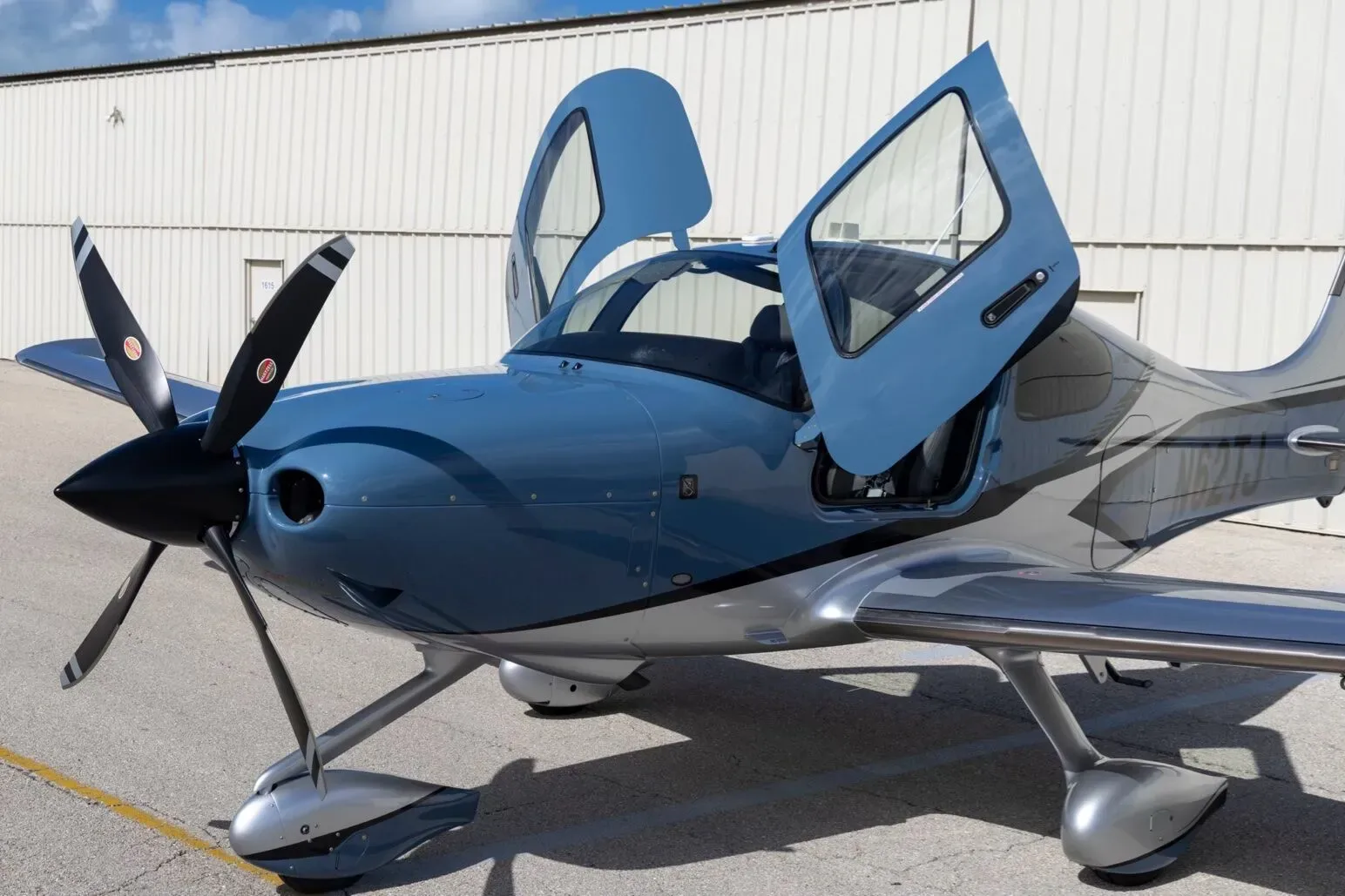 A close-up front view of the blue and silver Cirrus SR22T aircraft with its gull-wing doors open.