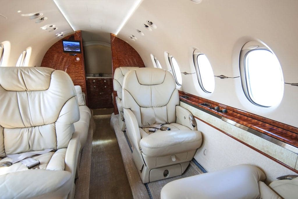 The elegant interior of a business jet, featuring cream leather seats, a plush carpet, and polished wood trim.
