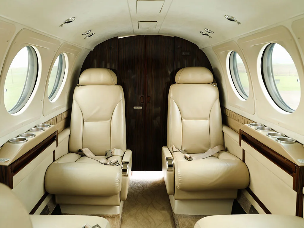 The interior cabin of a private jet with two beige leather seats facing a dark wood partition.