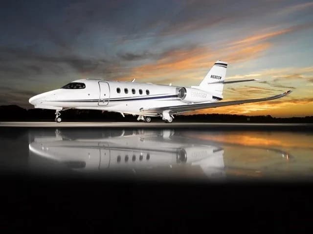 A white business jet, N680SW, with blue and grey stripes on the tail, parked on a wet tarmac at sunset.