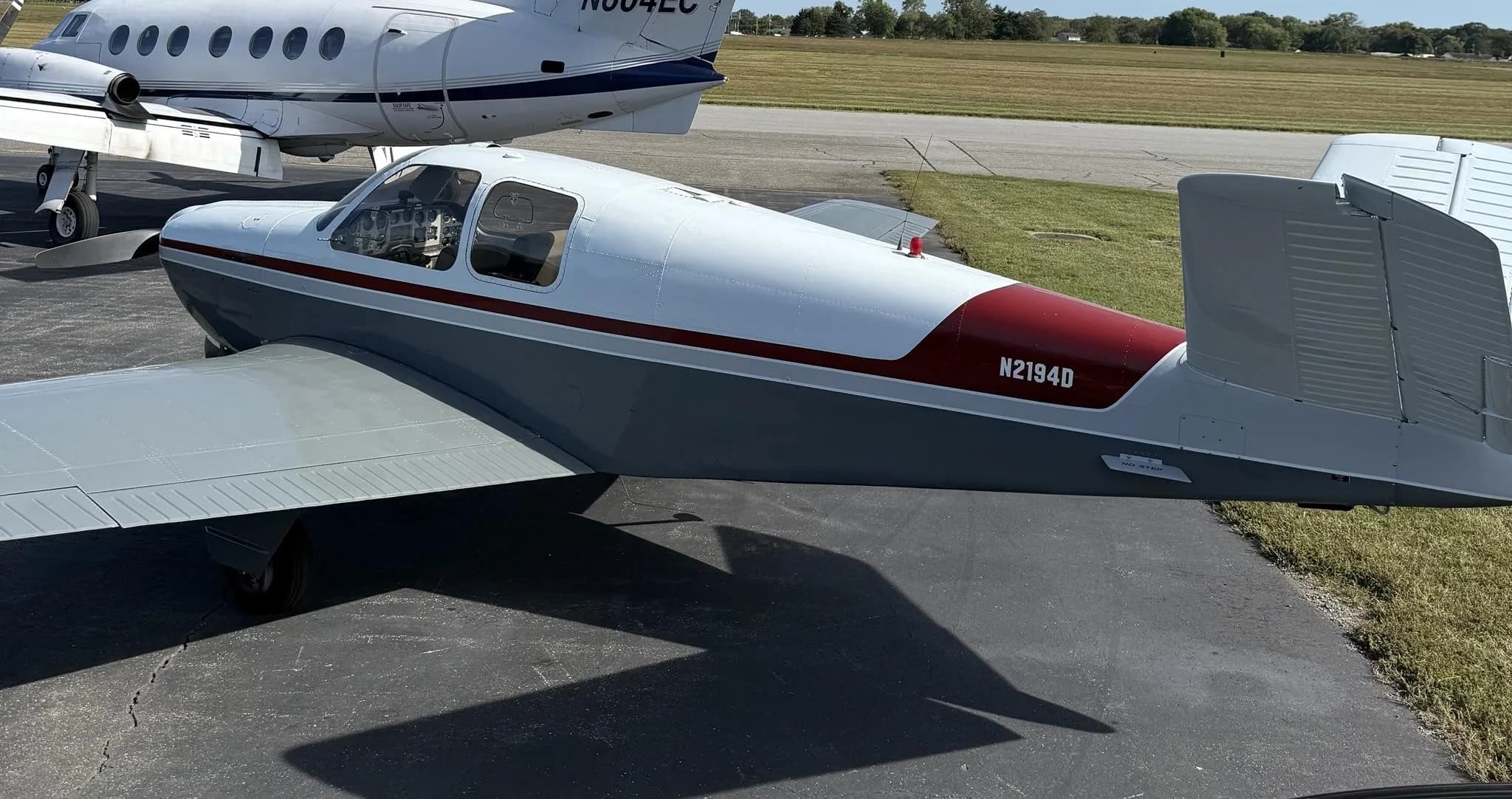 A grey and white single-engine aircraft with a red stripe on the tail, registration N2194D, parked on an asphalt ramp with another white aircraft behind it.