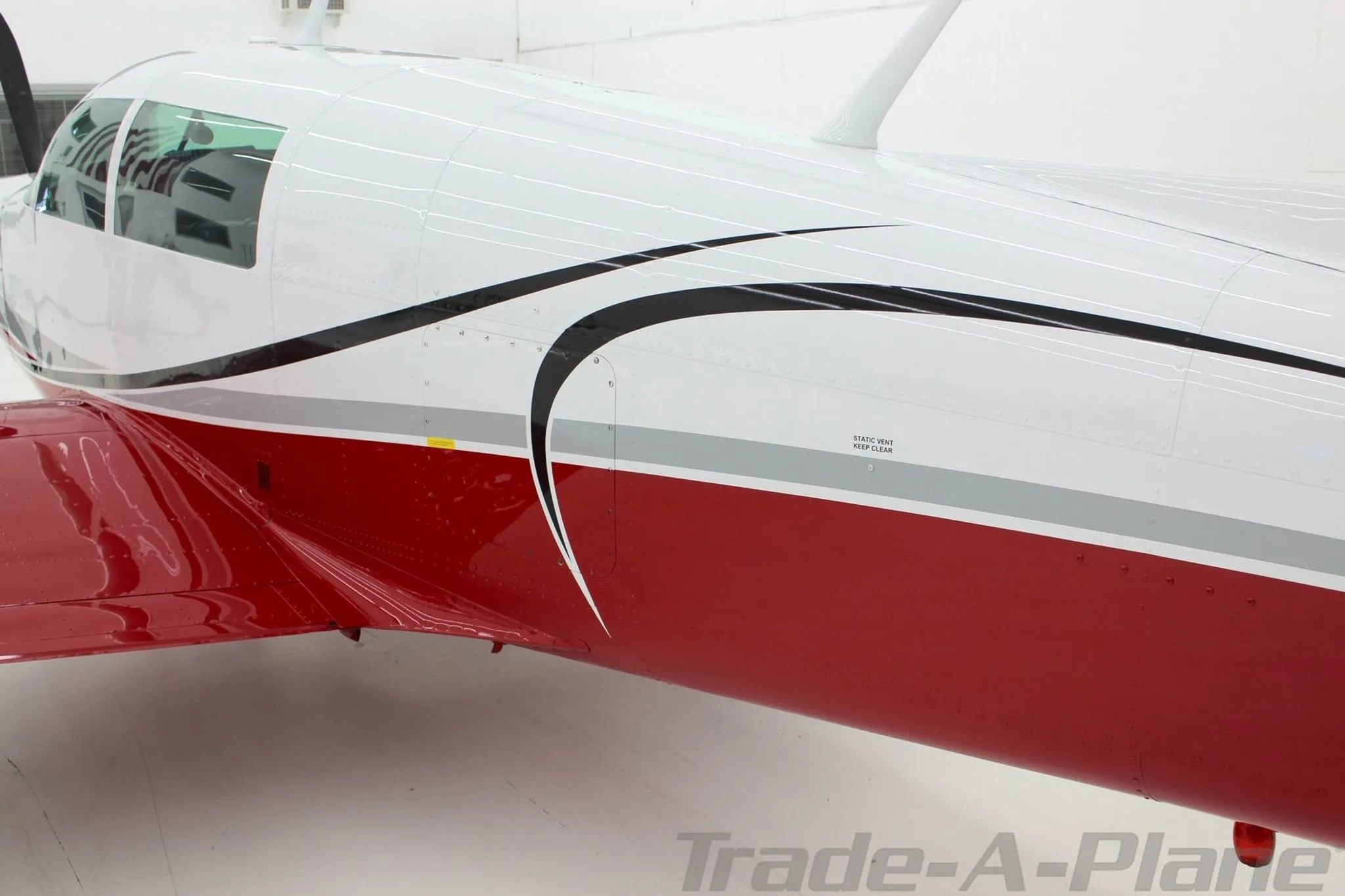 A close-up of the fuselage side of the Mooney N1039B, showing the red, white, and grey paint scheme.