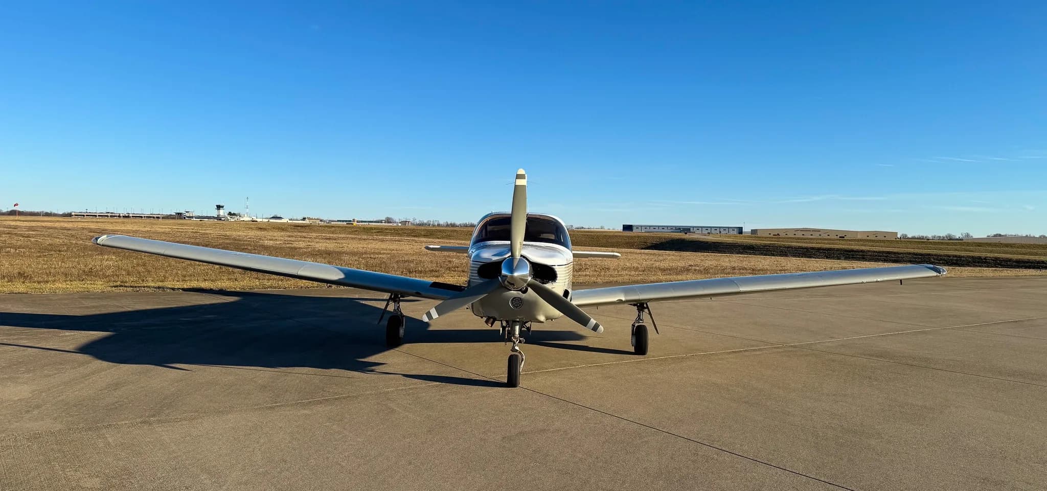 A head-on view of a white Piper Saratoga SP (N1622P) with grey stripes on an airfield.