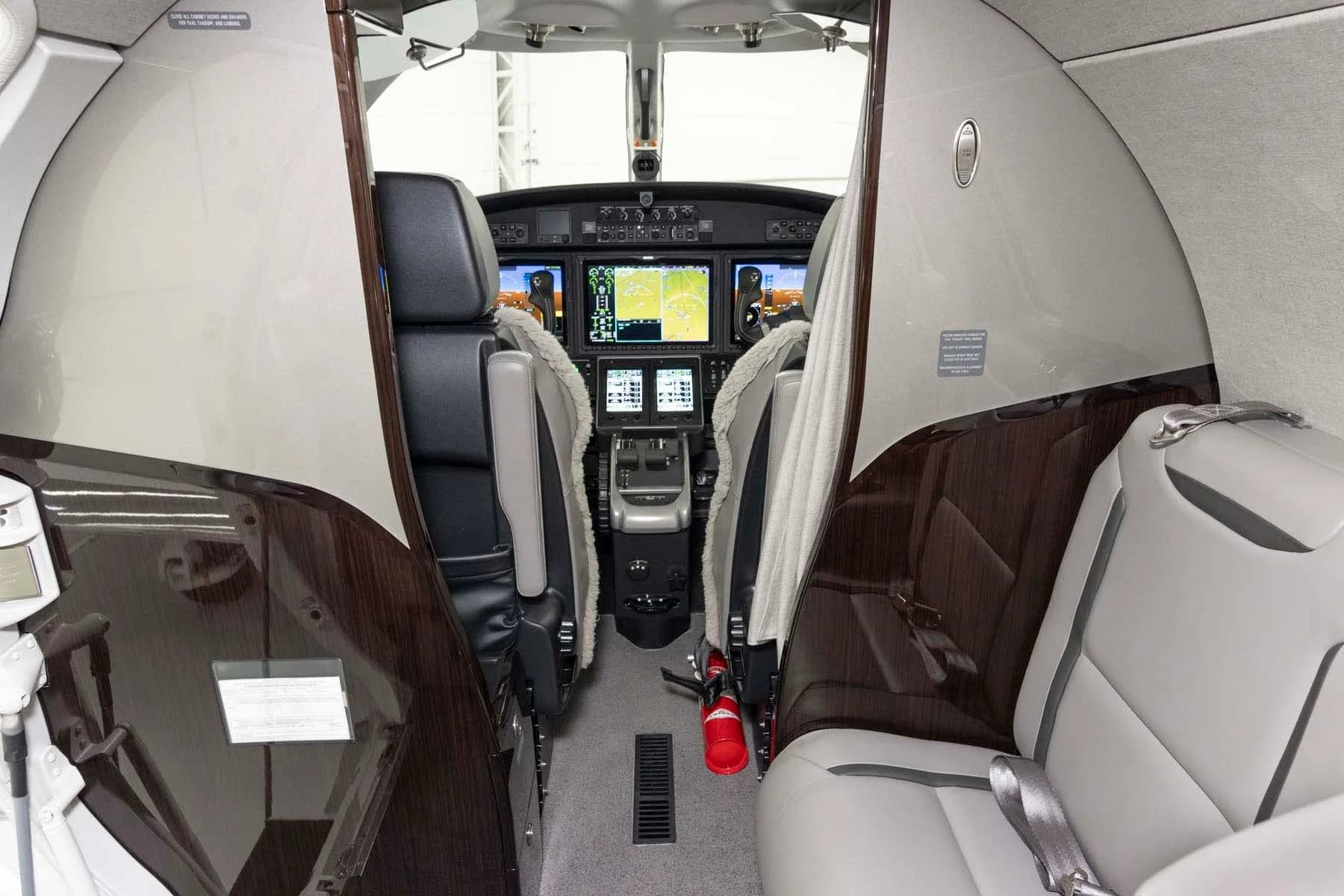 A view from the private jet's cabin looking into the modern cockpit with multiple display screens.