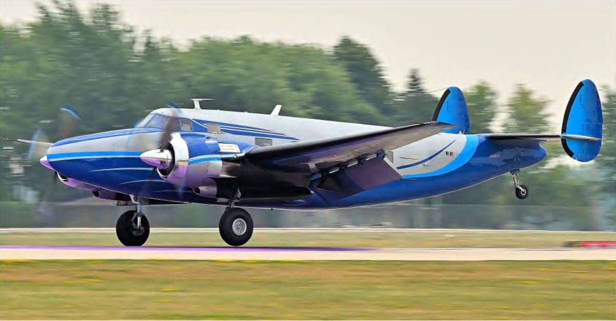 A blue and silver Beechcraft Model 18 landing on a runway.