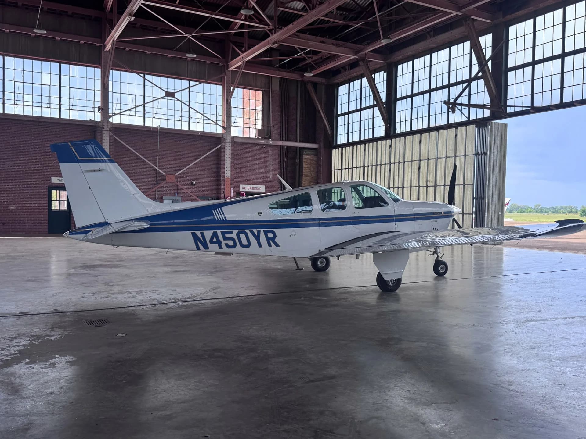 A side view of the white and blue Beechcraft Bonanza F33A aircraft with registration N450YR in a hangar.