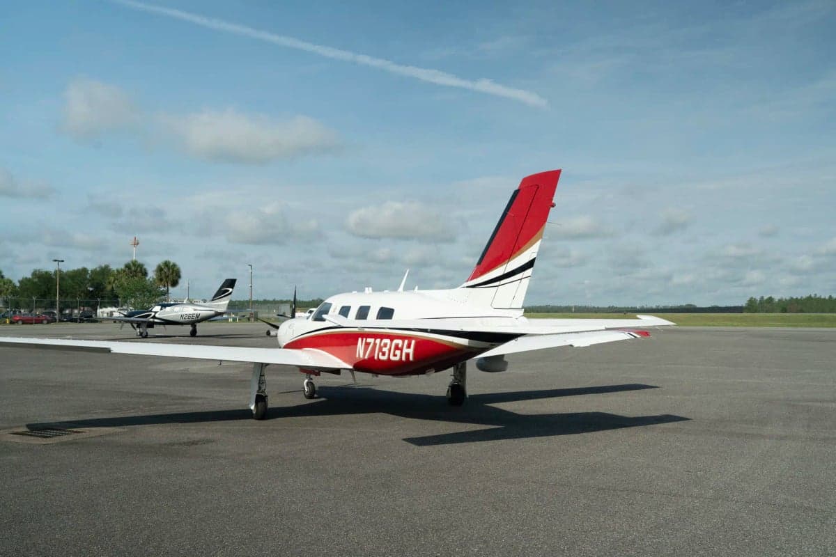A white and red Piper M500 aircraft with registration N713GH viewed from the rear on an asphalt tarmac with another small plane in the distance.