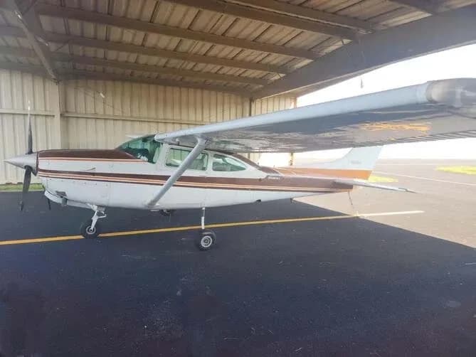 A white and brown Cessna Skylane RG II aircraft parked under an open-sided hangar.