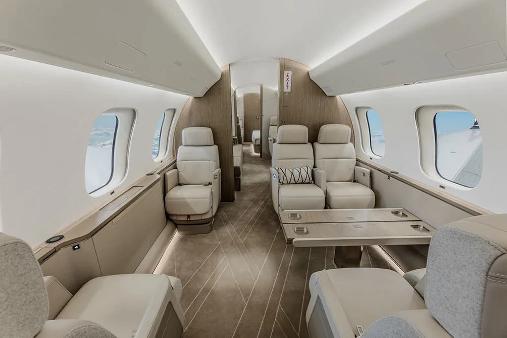A private jet cabin interior featuring beige seats, a fold-out table, and light wood accents.