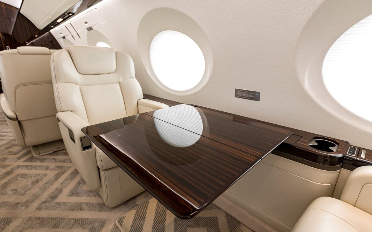 A close-up of the Gulfstream G500 cabin featuring cream-colored leather seats and a dark wood table.
