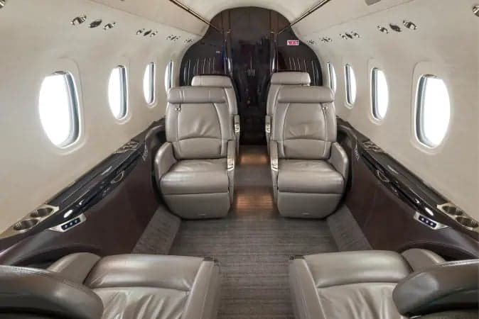 Aircraft cabin interior with leather seats and dark wood trim.