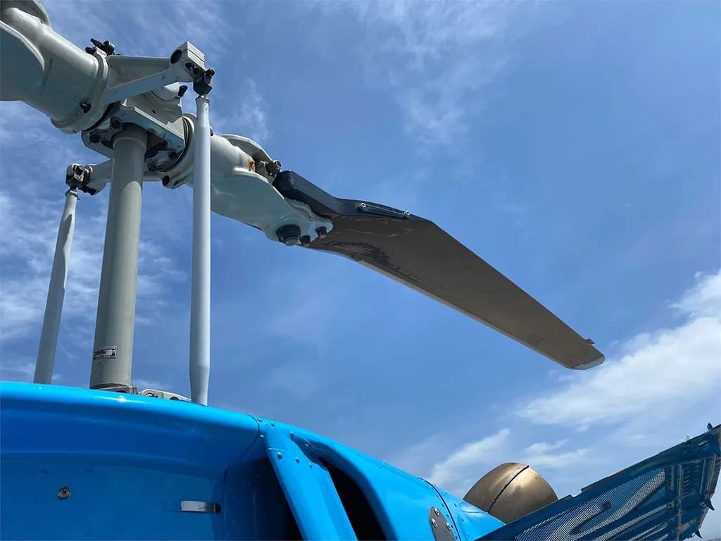 A close-up view of the main rotor assembly of the blue Bell 206 helicopter against a clear blue sky.