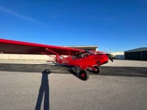 A red aircraft is parked on the tarmac under a blue sky.
