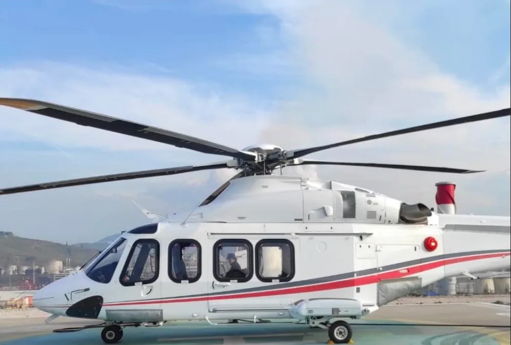 A white and red AgustaWestland AW139 helicopter is parked on a helipad.
