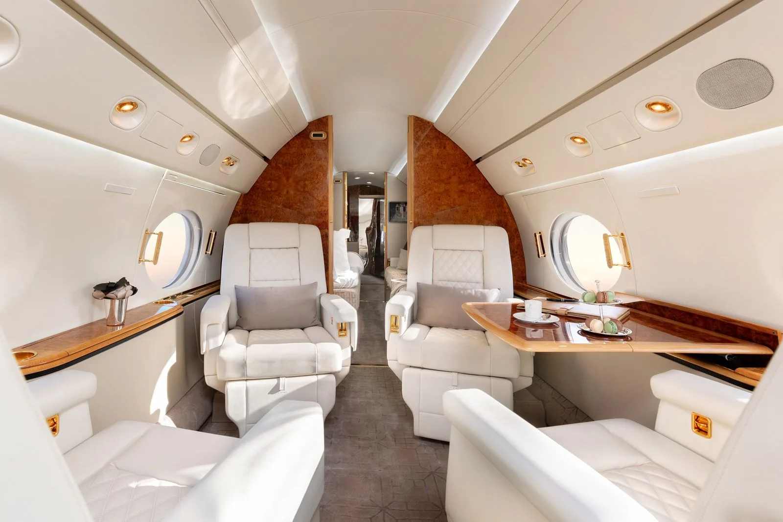 A view down the aisle of a luxurious aircraft cabin with white leather seats and wood accents.