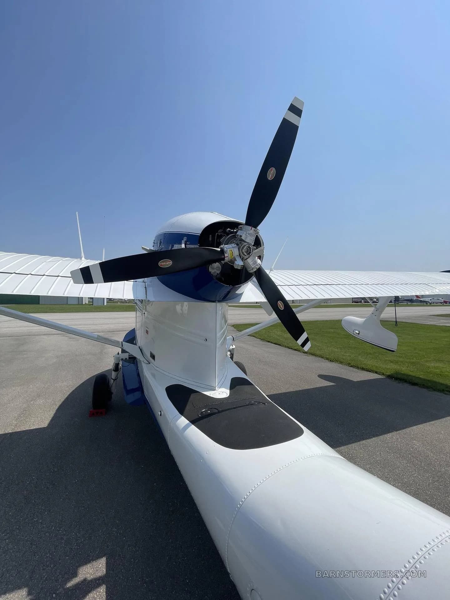 A close-up view of the front of a white and blue amphibious aircraft, showing its propeller and engine cowling.