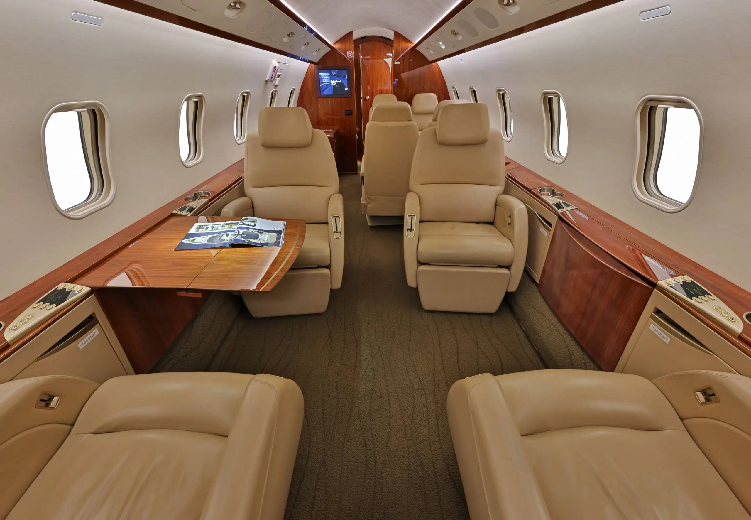 View of the luxurious beige leather seats and polished wood tables in the aircraft cabin.