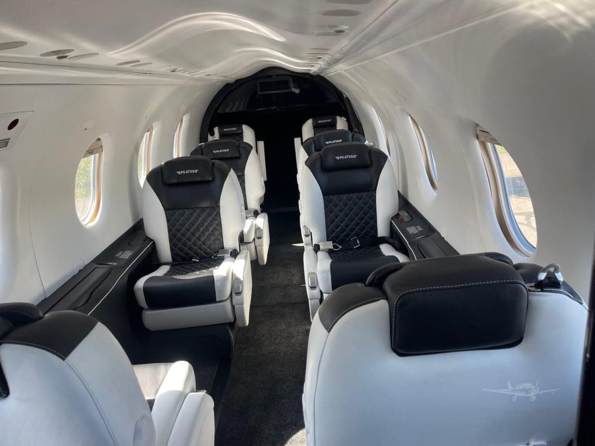The aircraft cabin features black and white quilted leather seats arranged in a passenger configuration.