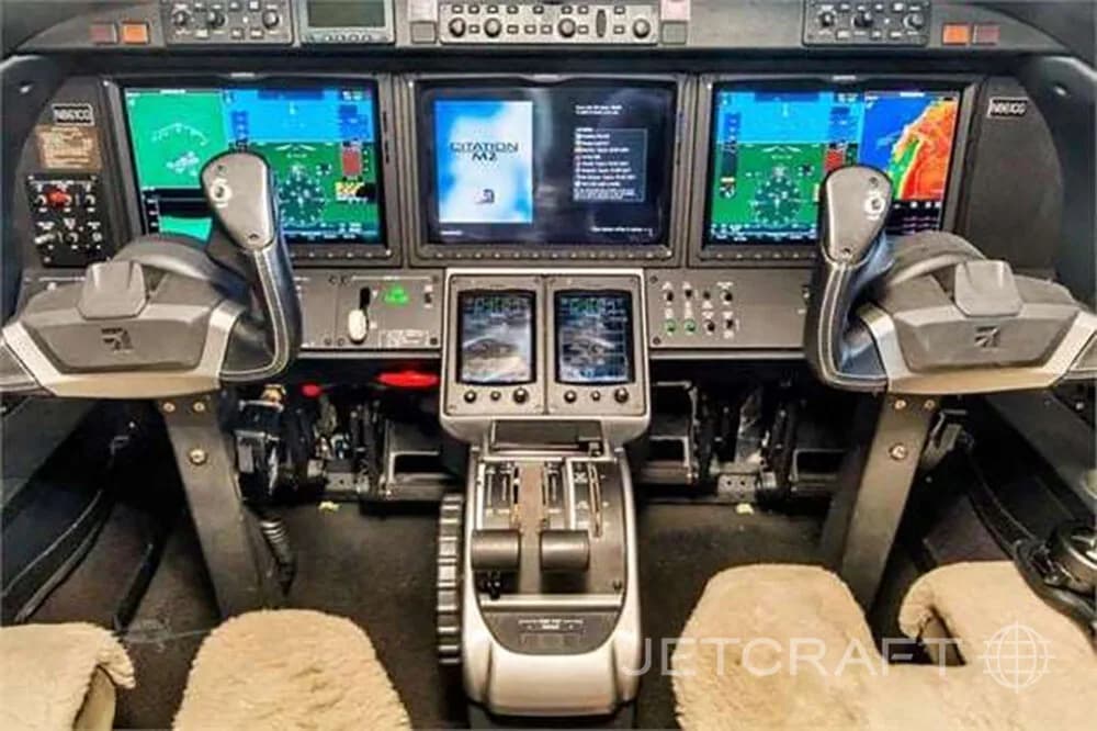 The cockpit of a Citation M2 jet, showing multiple glass displays and control yokes.