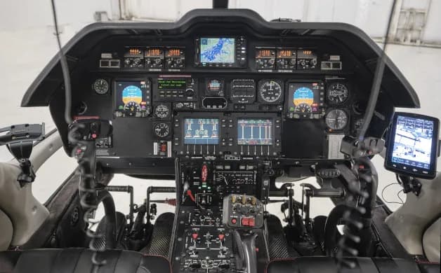 The helicopter cockpit displays multiple screens, analog gauges, and flight controls.