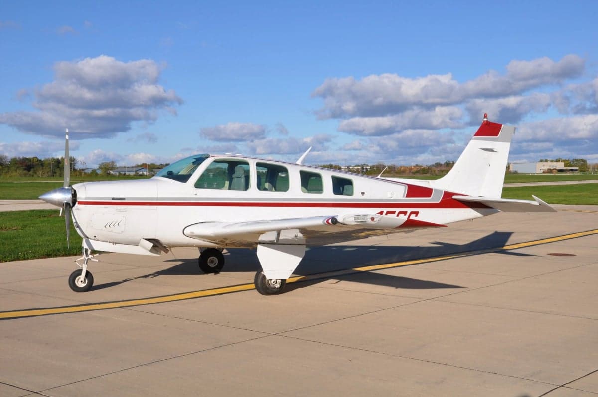 A Beechcraft Bonanza aircraft with a red and white paint scheme, parked on the tarmac.