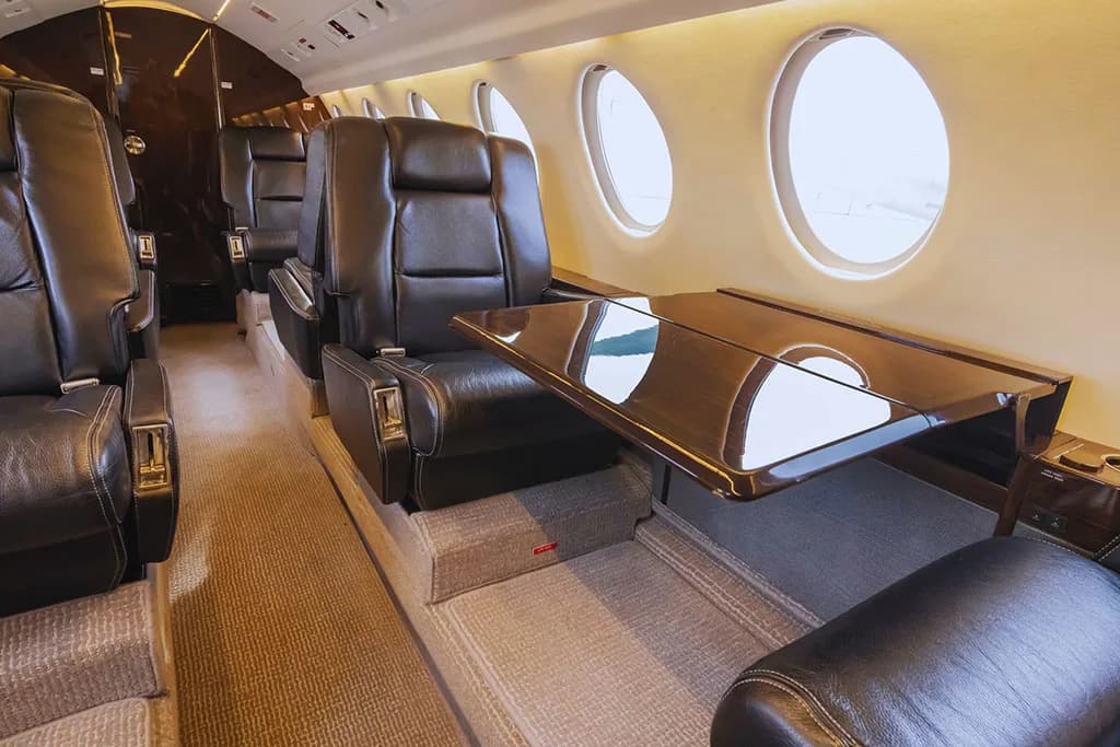 A close-up of the aircraft's interior, showing black leather seats and a polished wooden table extended between them.