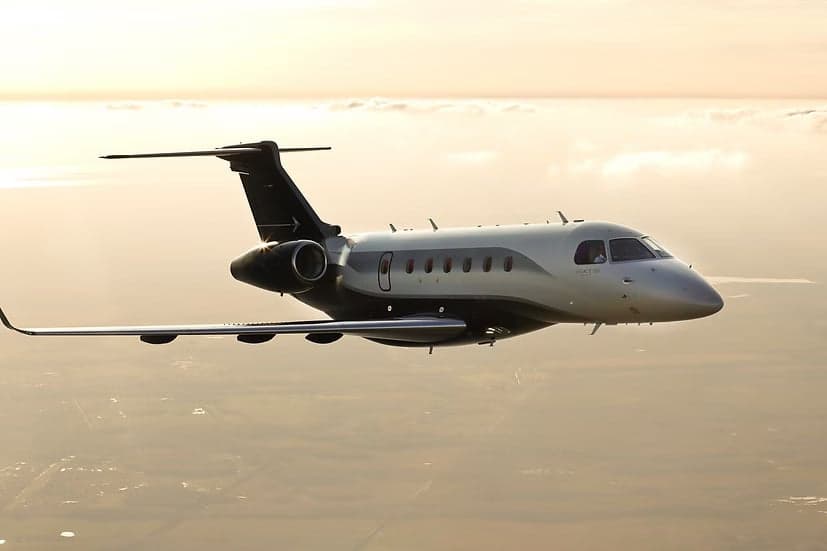 A Embraer Phenom 300E in flight against a sunset sky.
