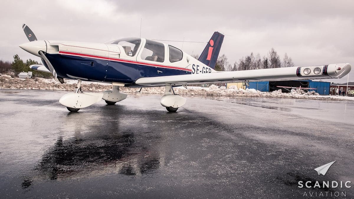 A blue and white aircraft is parked on a wet tarmac.