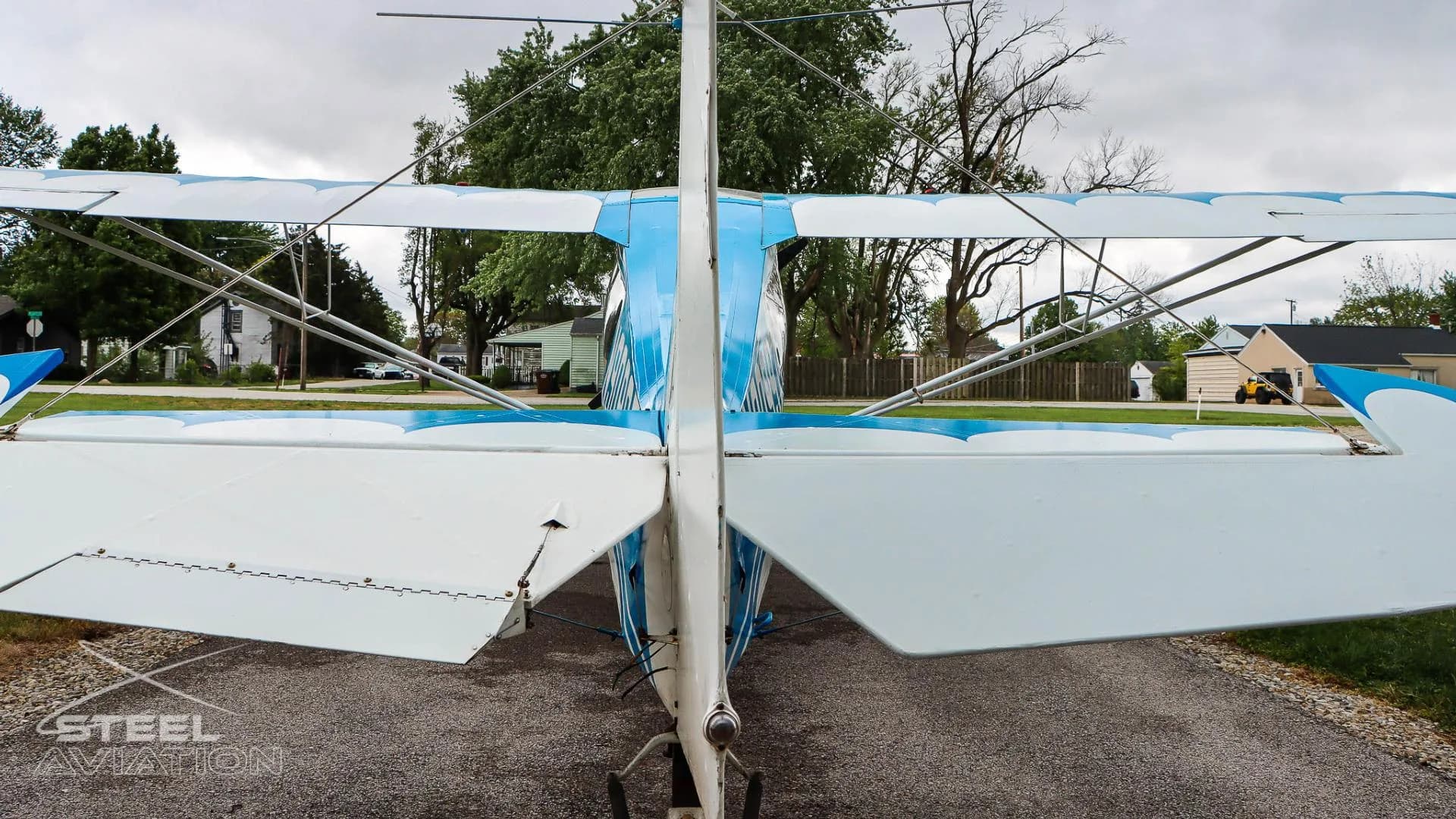 Rear view of a white and blue Bellanca 7GCBC Citabria aircraft, showing the tail and wings from behind.