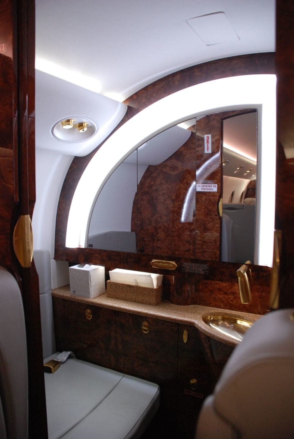 A luxurious aircraft lavatory with a large mirror, sink, and wood paneling.