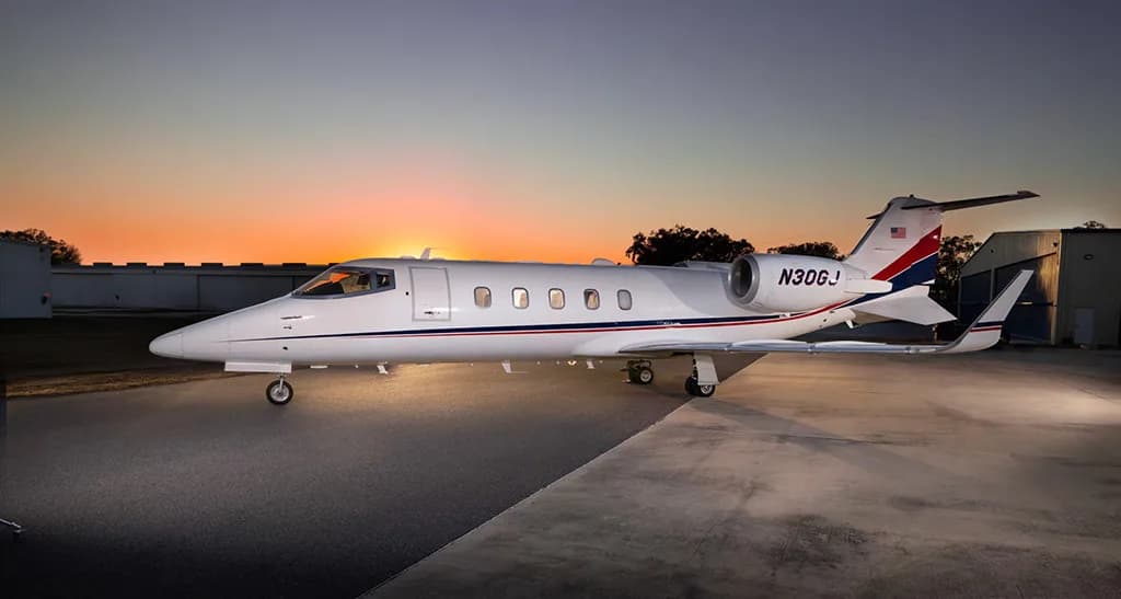 A white Learjet with red and blue tail stripes, registration N30GJ, parked on an airfield at sunset.