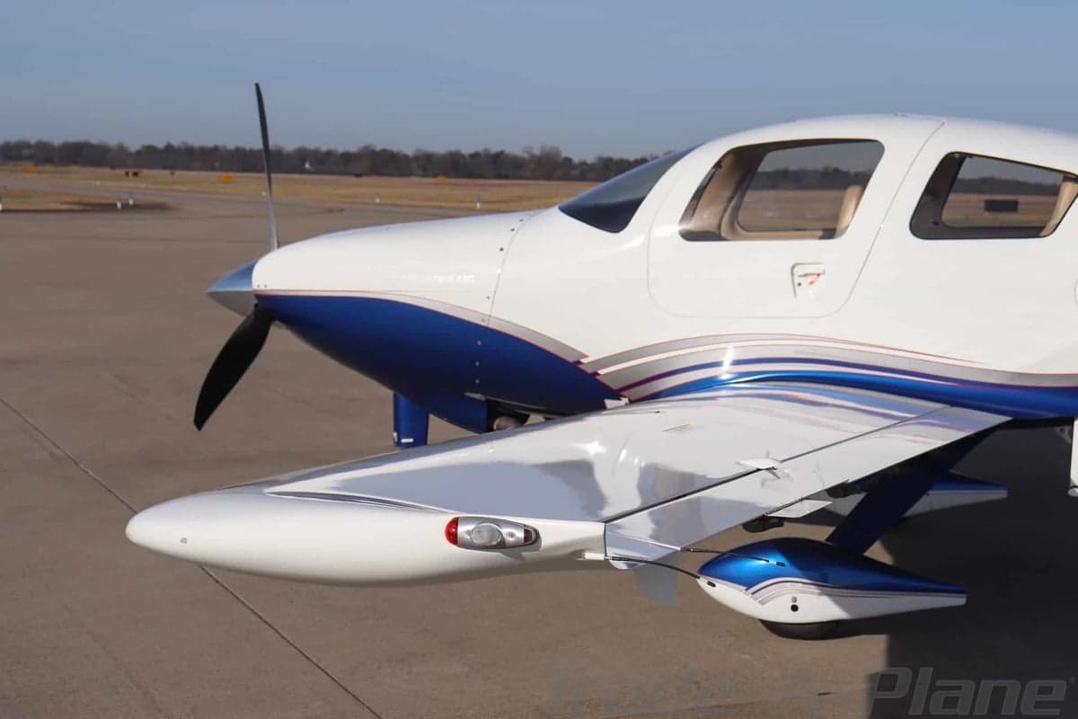 Front-right view of a white and blue Columbia 400 aircraft with a propeller on an airfield.