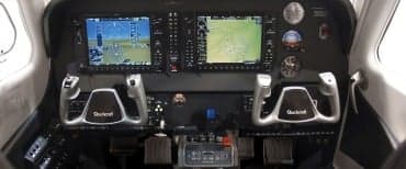 A Bonanza G36 aircraft in flight over a lake and wooded area.