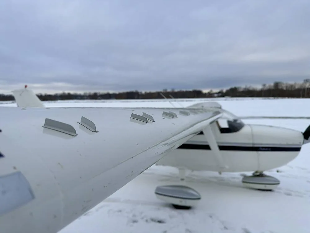 Close-up view of the wing and front fuselage of a white Cessna 172 N246TB in a snowy setting.