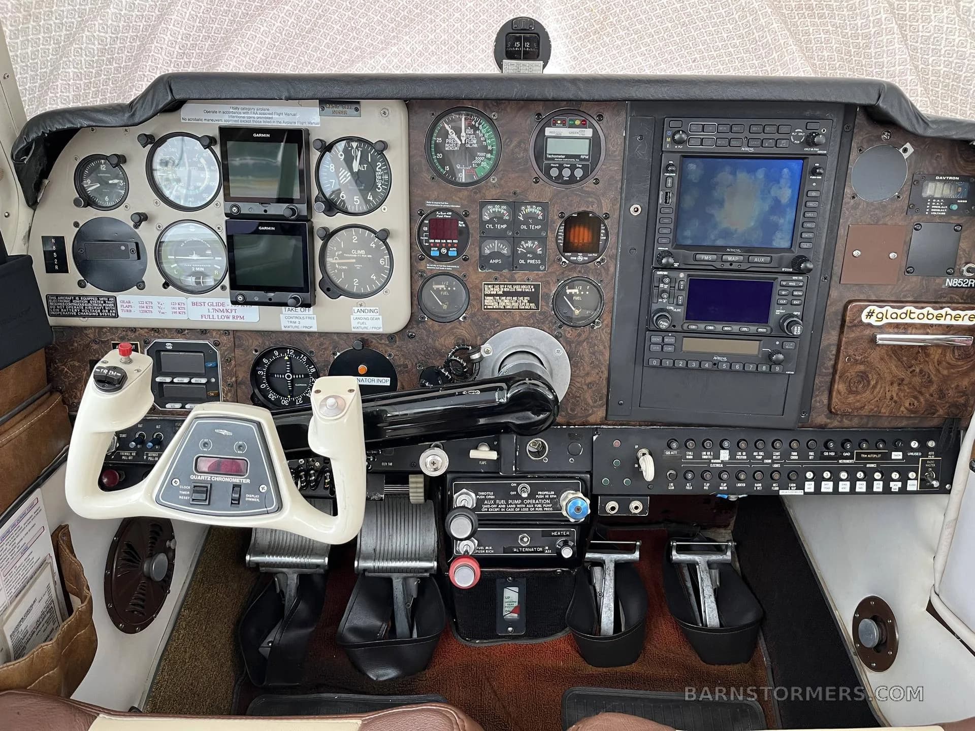 The cockpit of a Beechcraft Bonanza, showing the instrument panel with analog gauges, two Garmin displays, and a white control yoke.