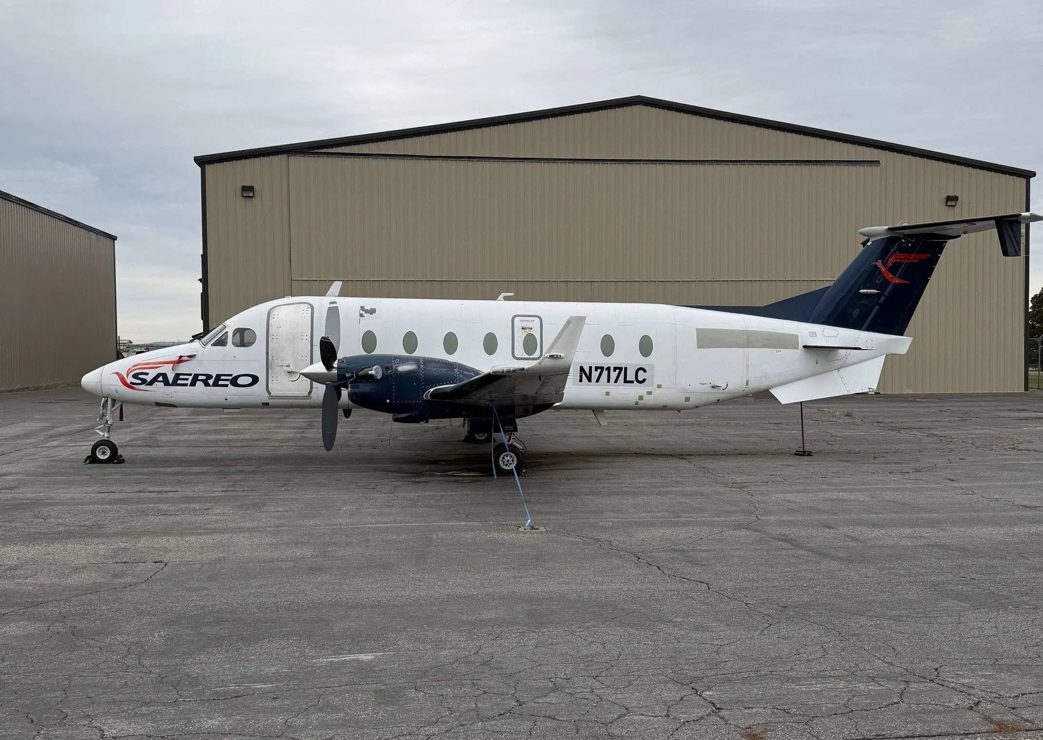 A Beechcraft 1900C with SAEREO livery is parked on the tarmac in front of a hangar.