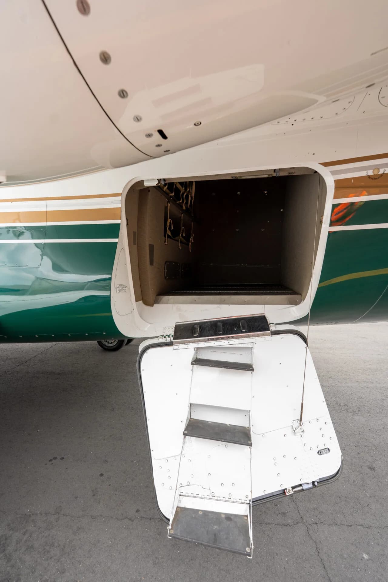 A close-up of the open rear cargo door of a white and green private jet with integrated stairs.