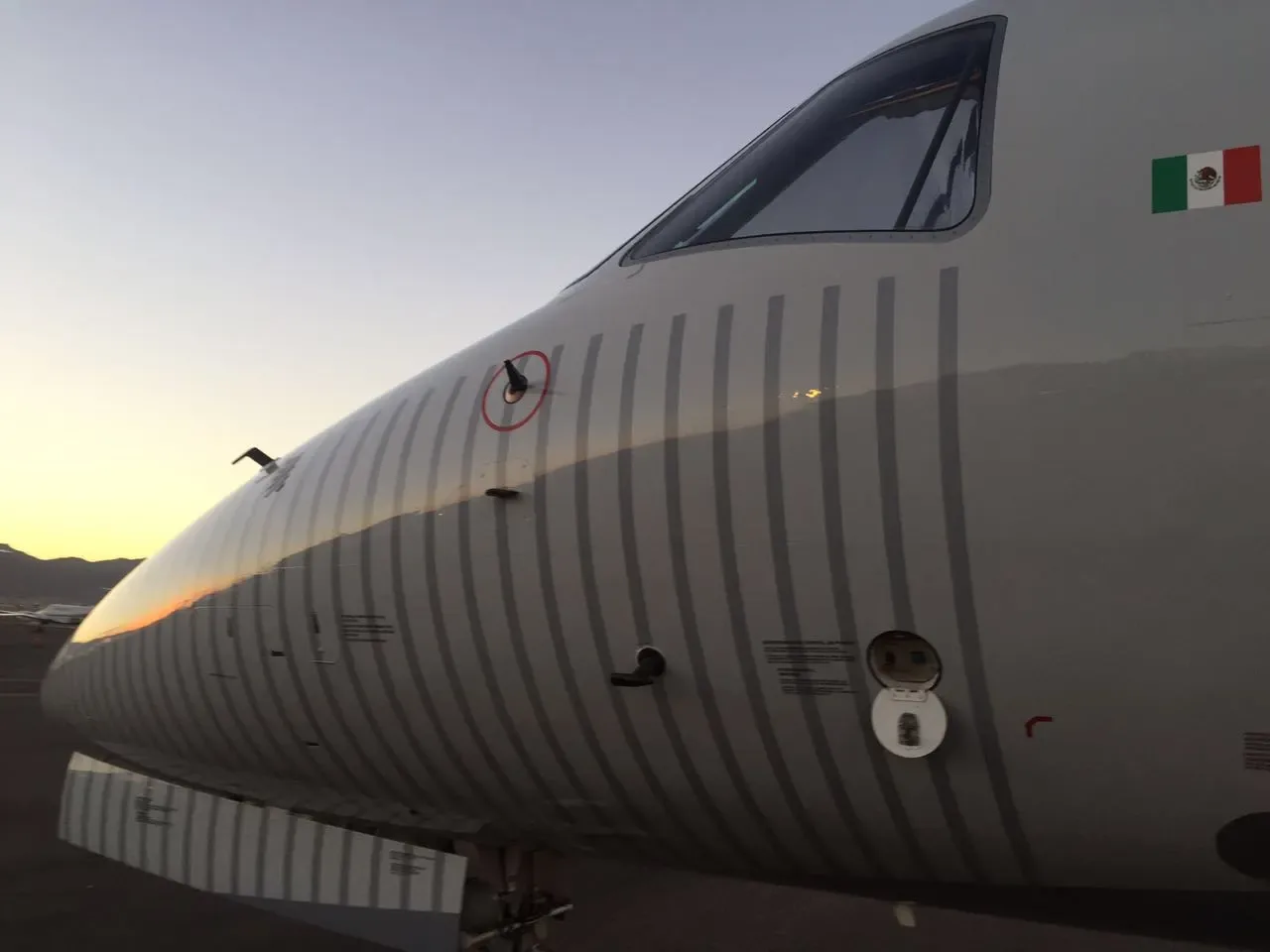 A close-up of the nose of a white Embraer Legacy 600 business jet, showing the Mexican flag.