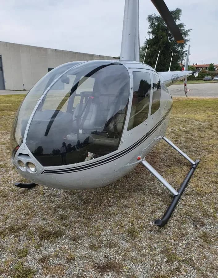 A close-up front-side view of a silver Robinson R44 helicopter on a gravel patch.