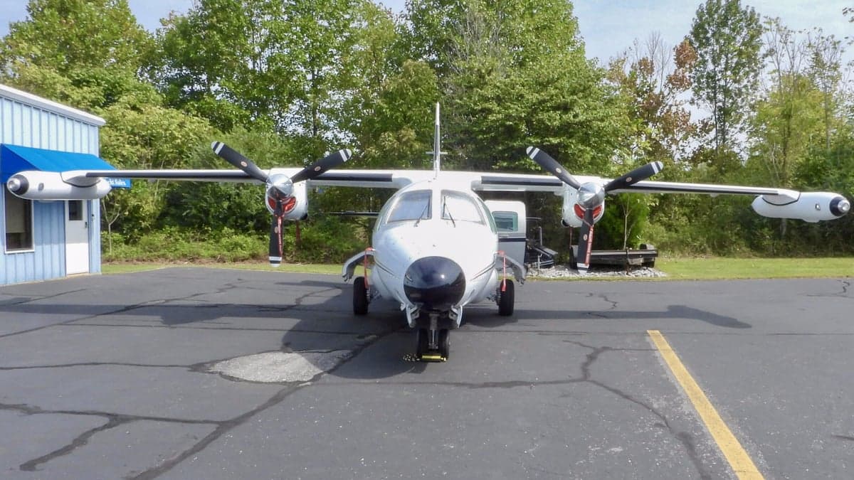 A white Mitsubishi MU-2 aircraft with a black nose, viewed from the front, parked on an asphalt ramp.