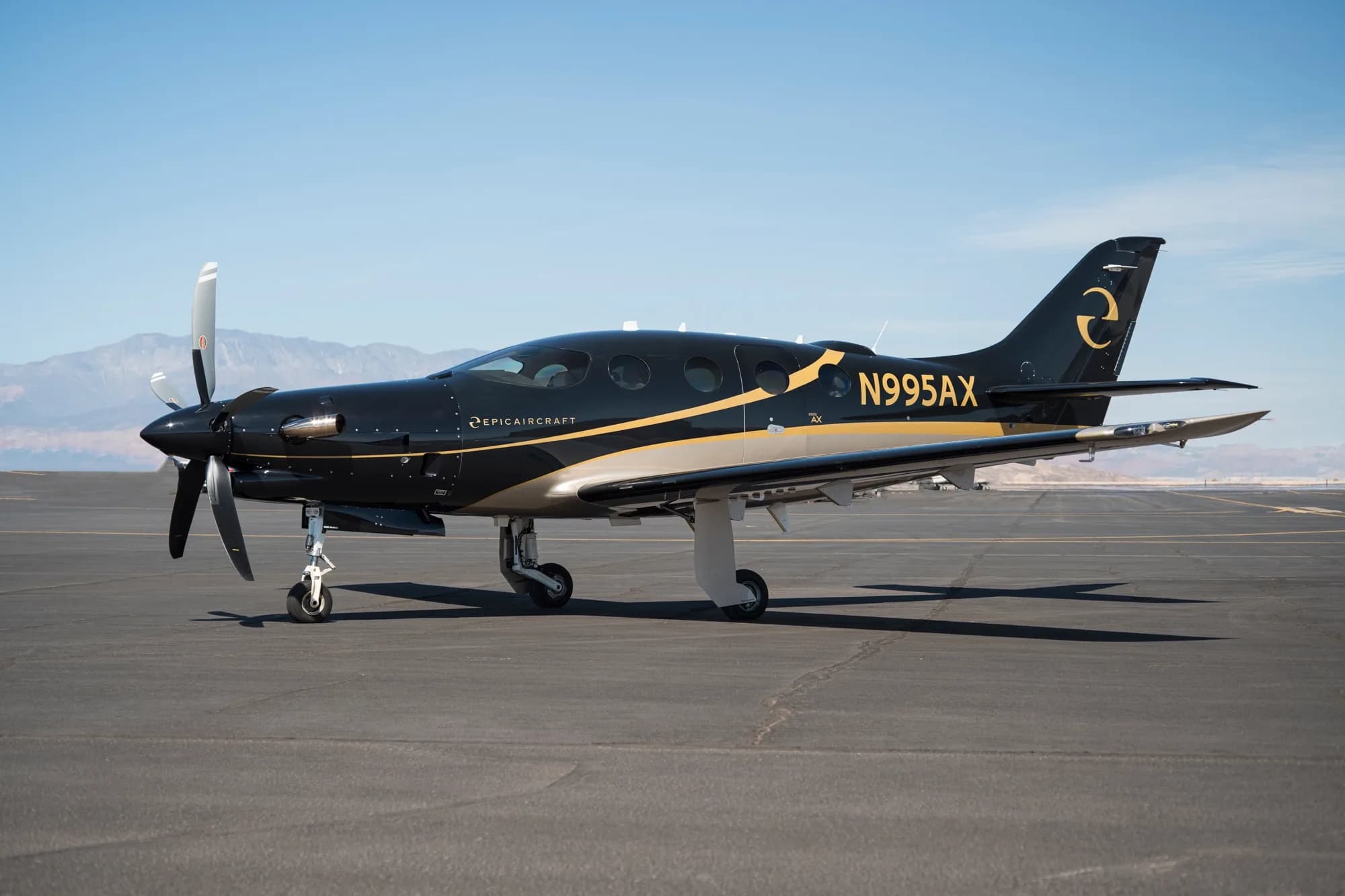 A black and gold Epic E1000 GX aircraft (N995AX) is parked on a tarmac under a clear blue sky.