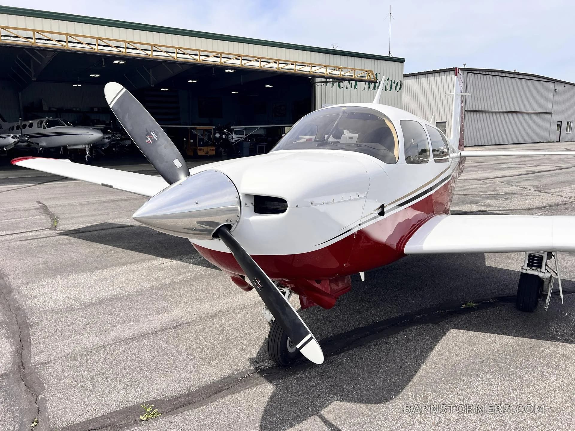 A front view of a white and red single-engine propeller aircraft with a hangar in the background.