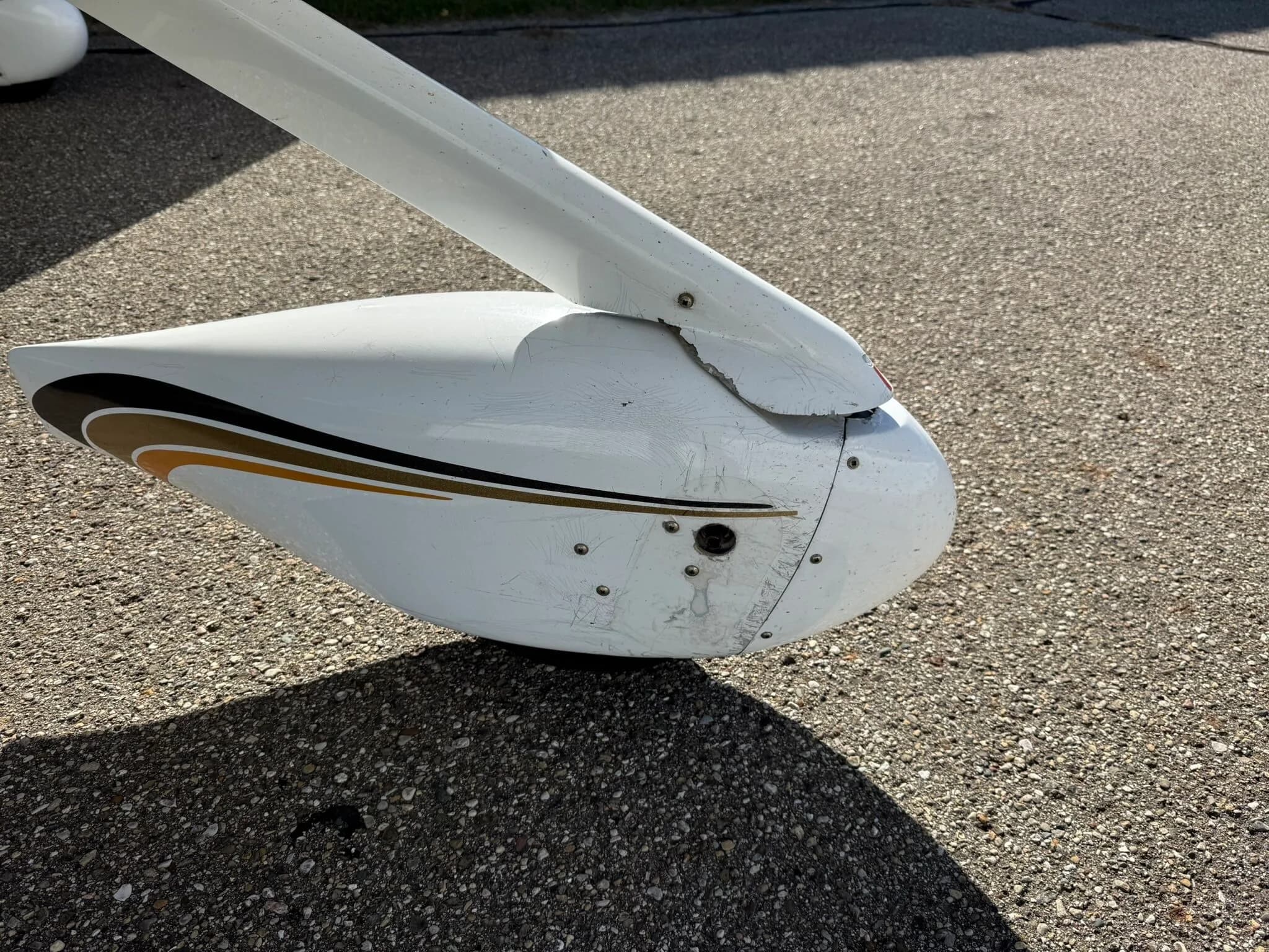 A close-up view of the white main landing gear fairing of the Cirrus SR20, showing black and gold stripe details and some wear.
