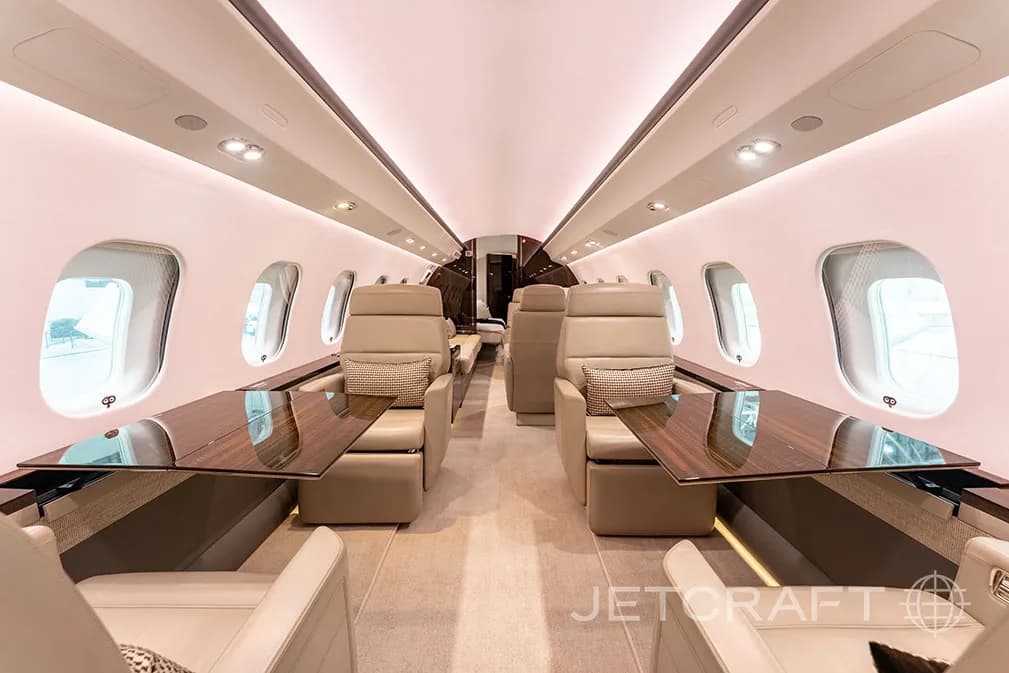 The luxurious cabin interior of a business jet, showing beige leather seats with wooden tables deployed between them.