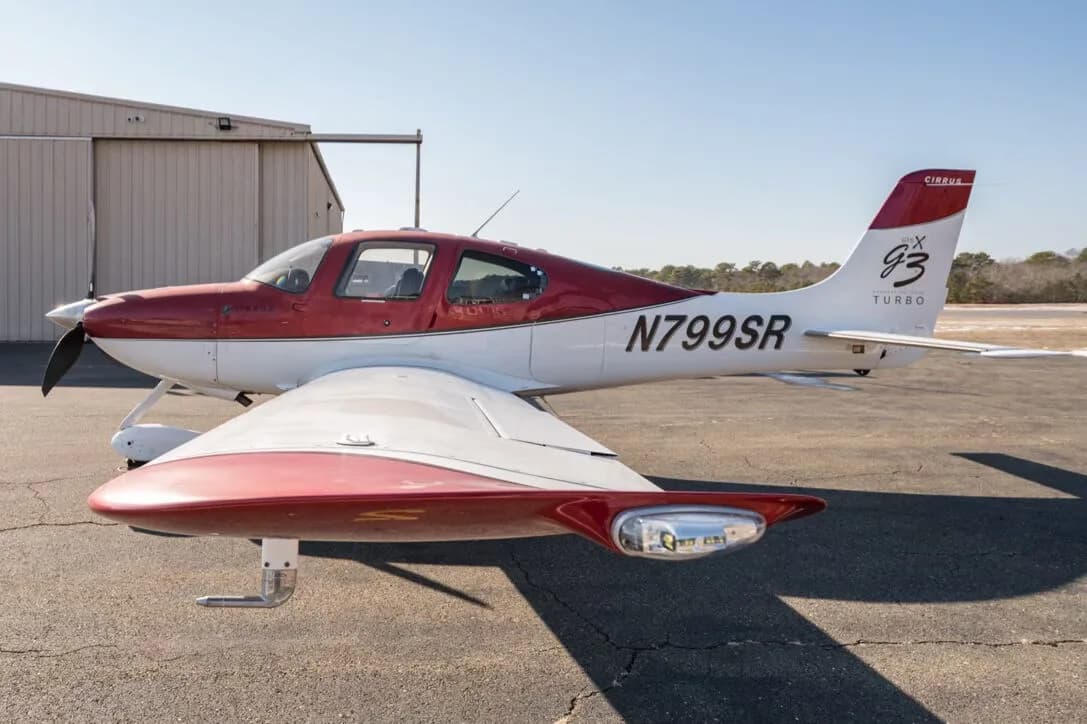 A red and white Cirrus SR22T aircraft, N799SR, parked on an tarmac with a hangar in the background.