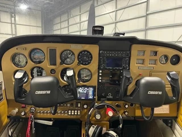 The cockpit of a Cessna aircraft features a gold-colored instrument panel with analog gauges and a modern GPS display.