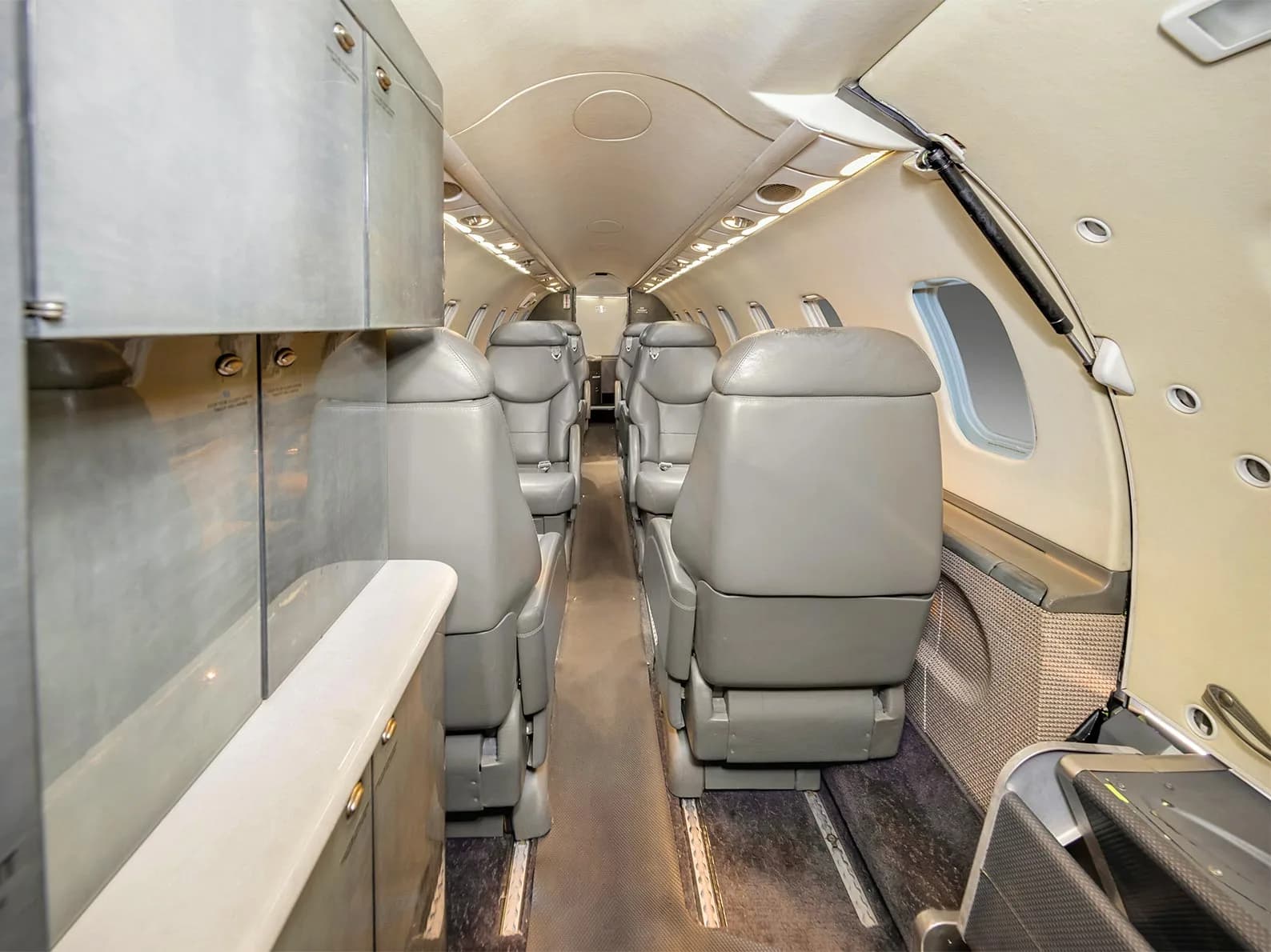 A view down the aisle of a business jet cabin with multiple rows of grey leather seats.